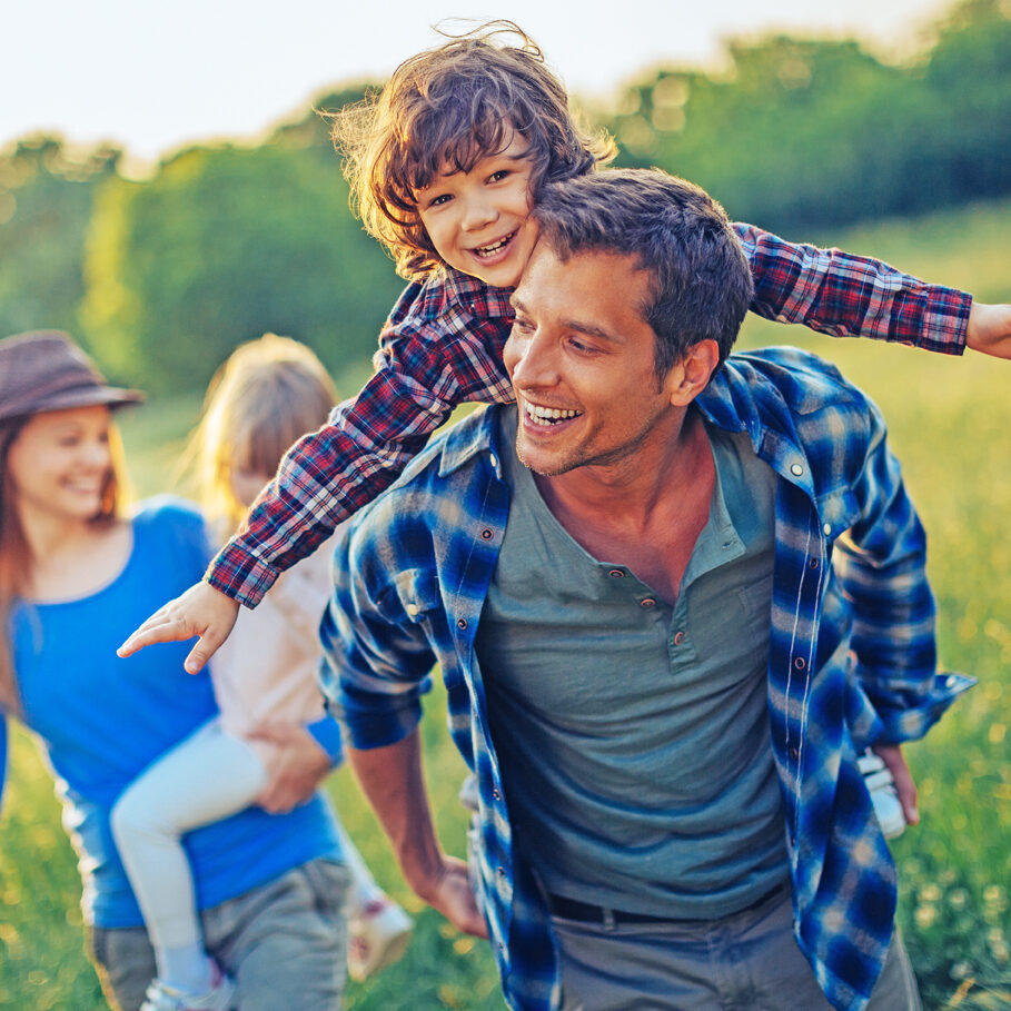 Picture of a young family going for a picnic, walking together threw high grass with the sun in their back.