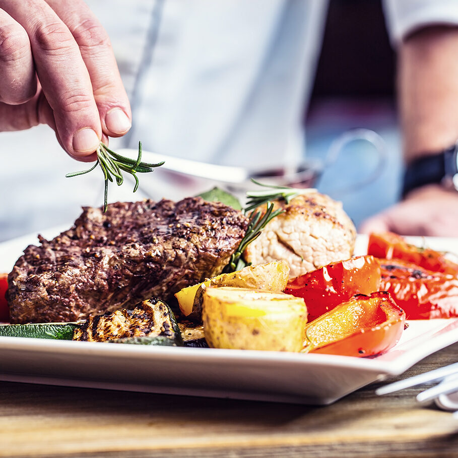 Chef in hotel or restaurant kitchen cooking only hands. Prepared beef steak with vegetable decoration.Chef in hotel or restaurant kitchen cooking only hands. Prepared beef steak with vegetable decoration.