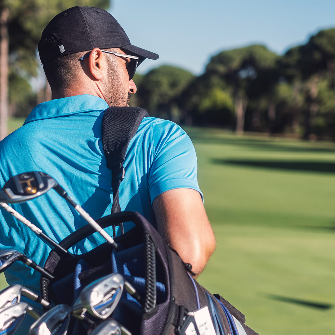 Young golfer walking by carrying golf bag in golf course.