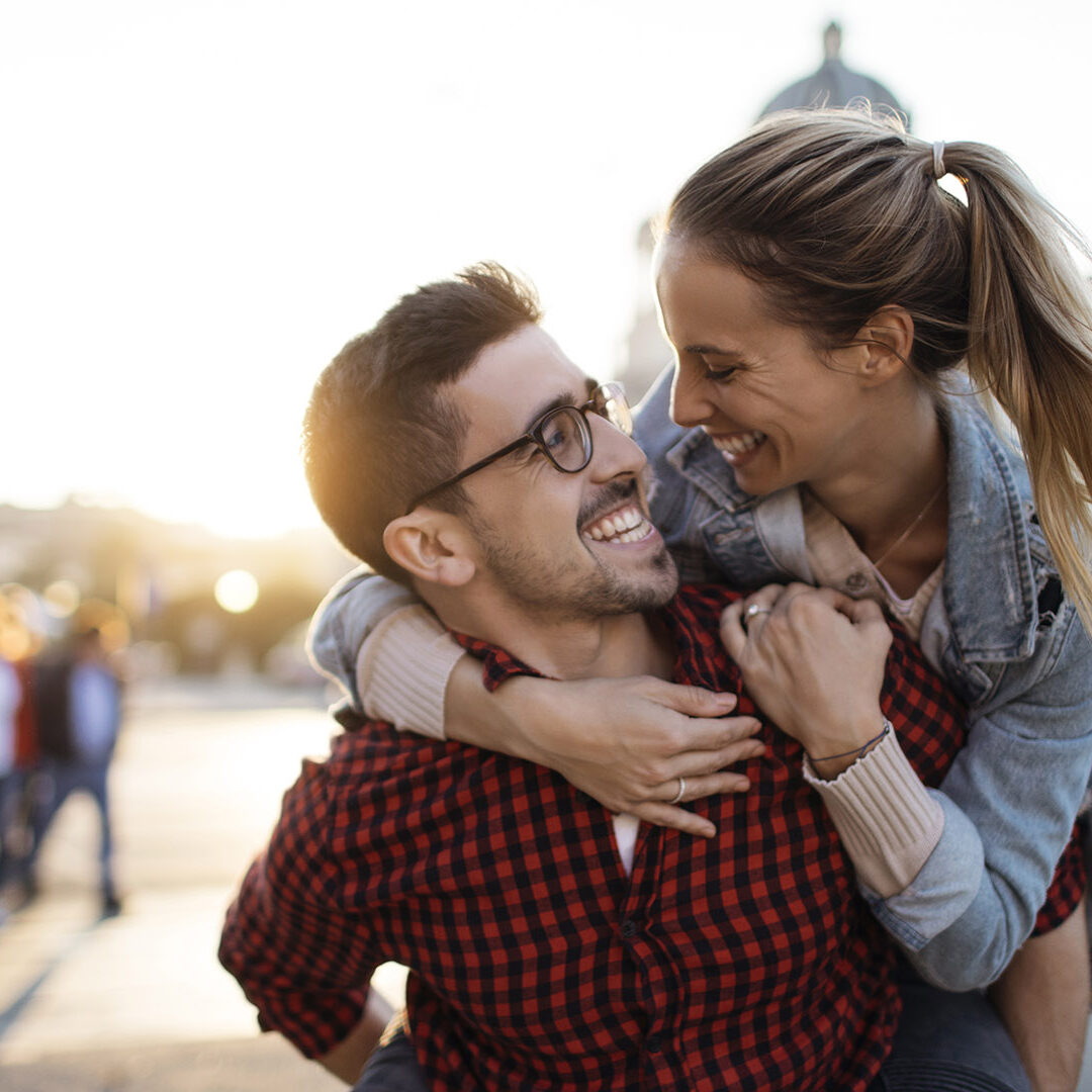 Happy boyfriend smiling and carrying girlfriend on his back outdoors