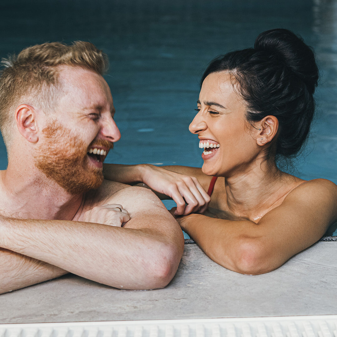 Smiling girlfriend and boyfriend in swimwear talking together in the swimming pool