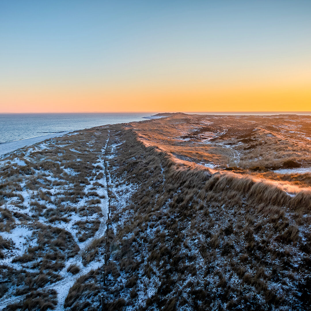 Red and white striped lighthouse situated on a coastal landscape at sunrise in winter. Lighthouse West-List on the Ellenbogen (the "Elbow"), the peninsula on northern coast of Sylt island in winter.