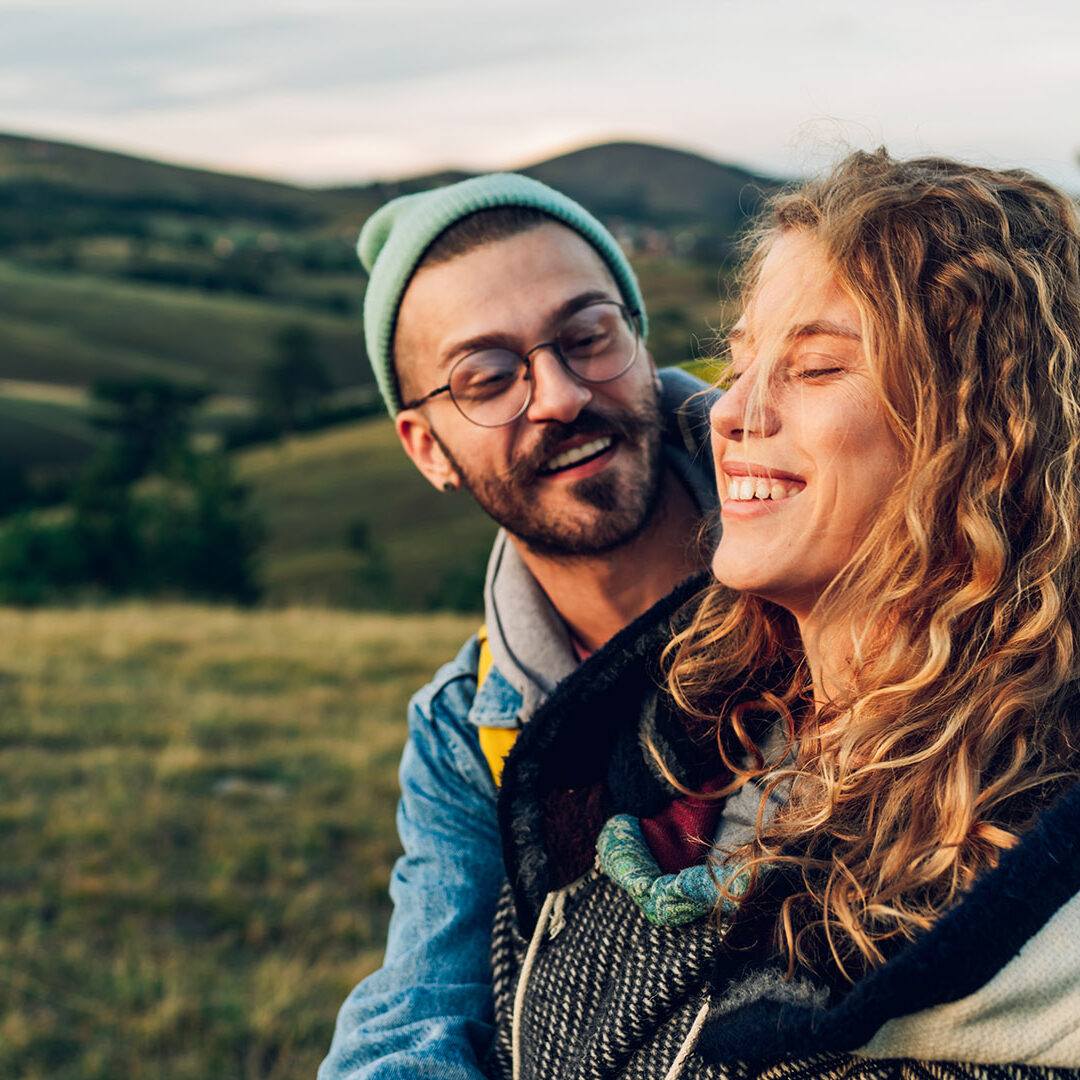 Happy couple in love embracing and following trail along grassy mountain ridge and having fun together while walking in the nature. Healthy lifestyle and romantic getaway. Focus on a smiling woman..